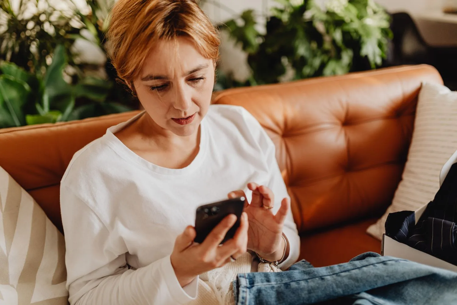 A woman on a leather sofa tapping her phone screen, as if pressing the contact button on a website
