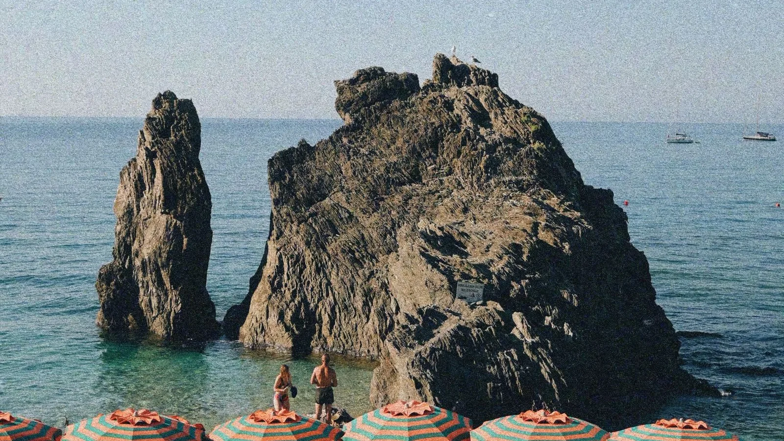 Roca arran de mar amb para-sols de ratlles en una platja mediterrània, l'estampa típica de les localitats de la Costa Brava com Blanes