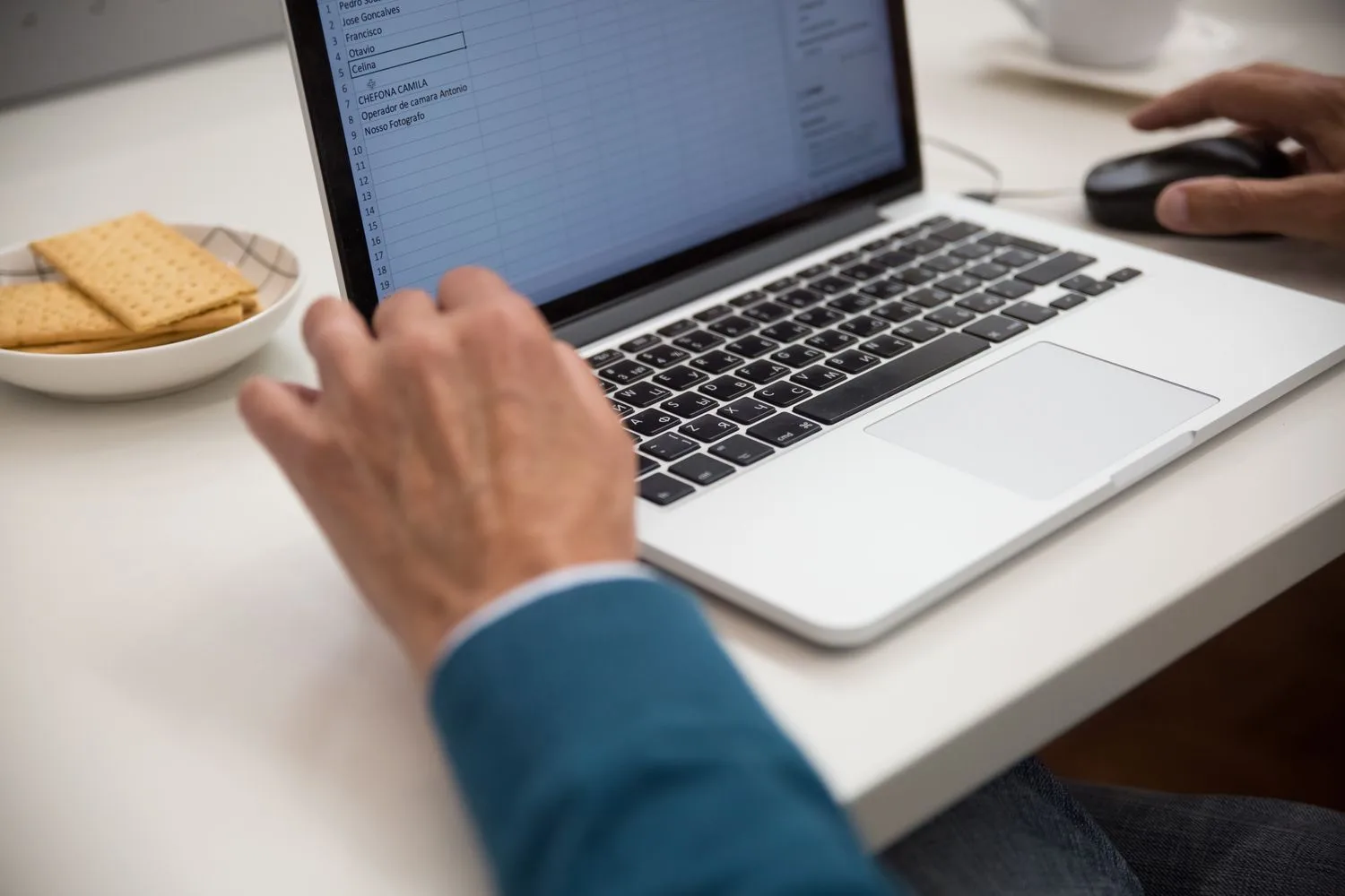 Hands working on a laptop spreadsheet, the file that ends up holding the process together