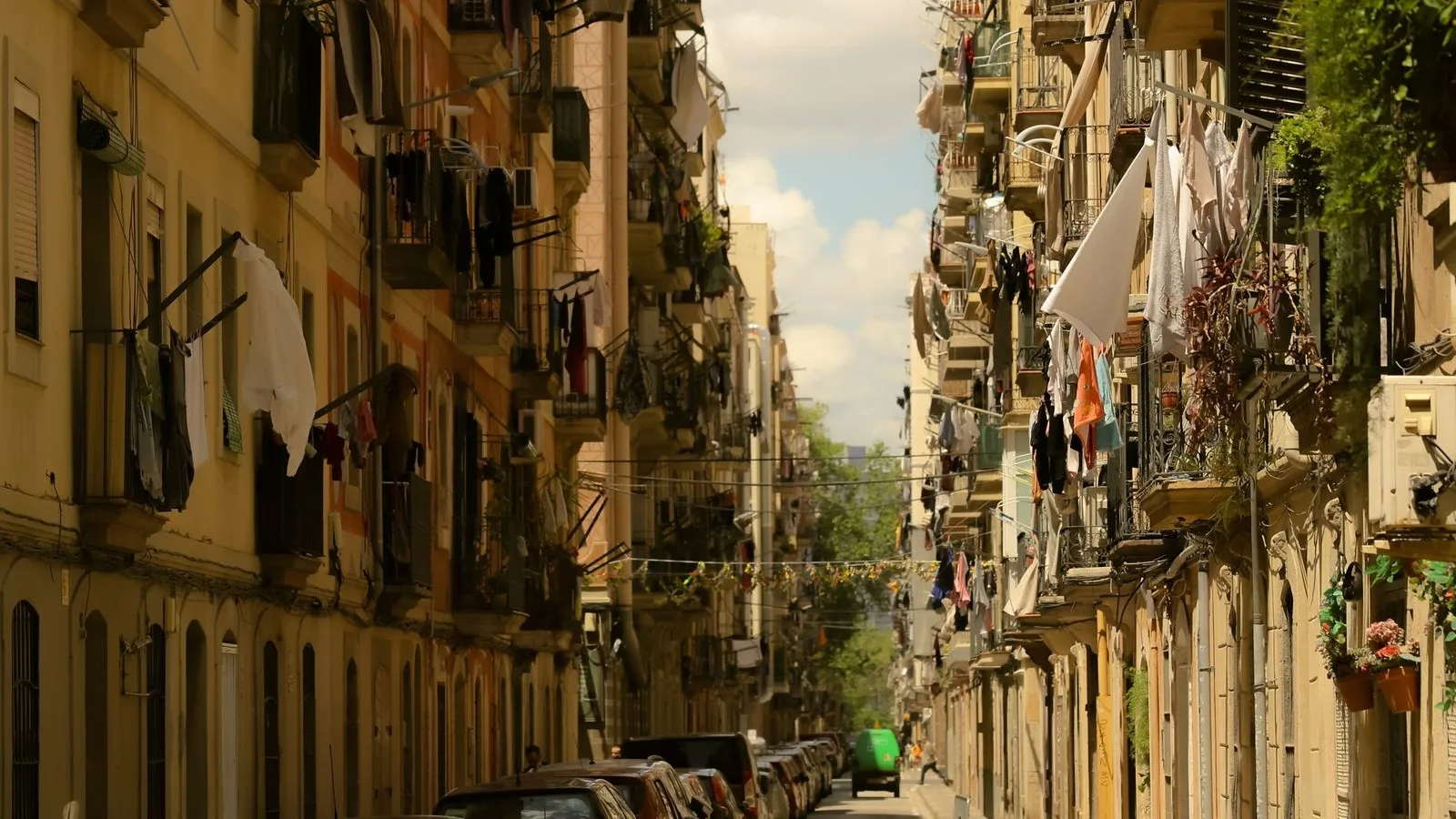 Narrow street in Barceloneta, Barcelona, with laundry on the balconies and festival garlands strung across it, the neighbourhood a local business's social media needs to reach