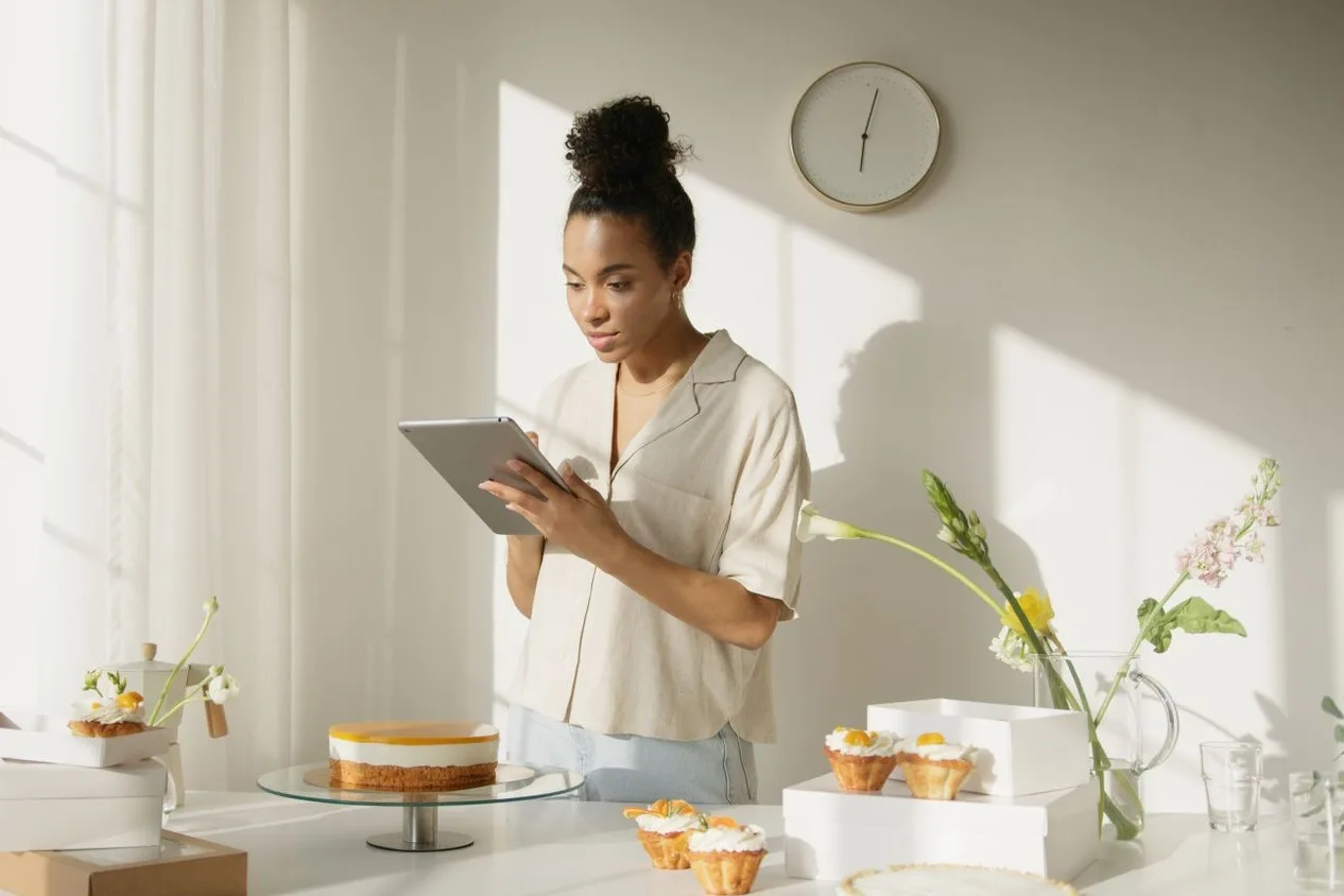 A pastry chef checks a tablet next to a cake and freshly made pastries, like someone going through a business's social media messages and stats