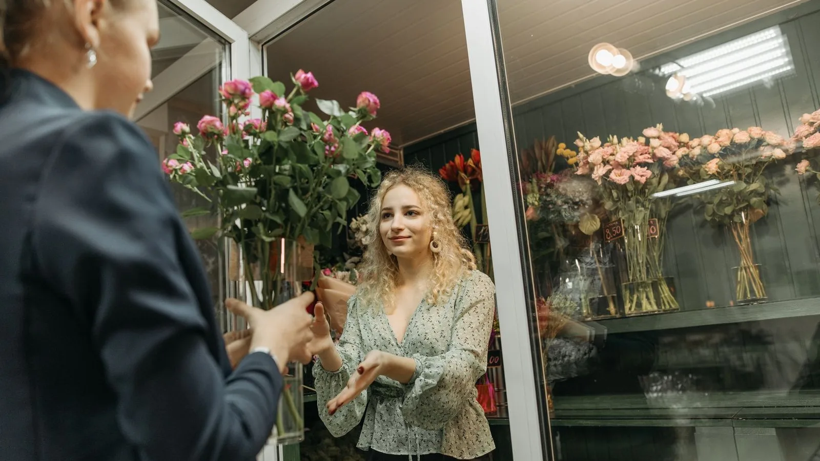 Florista atenent una clienta a la porta del seu comerç de barri