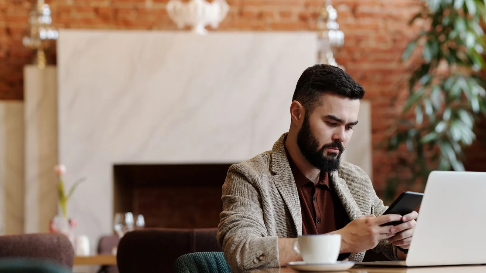 A person with a laptop and phone in a café, about to take the step and get in touch with a business