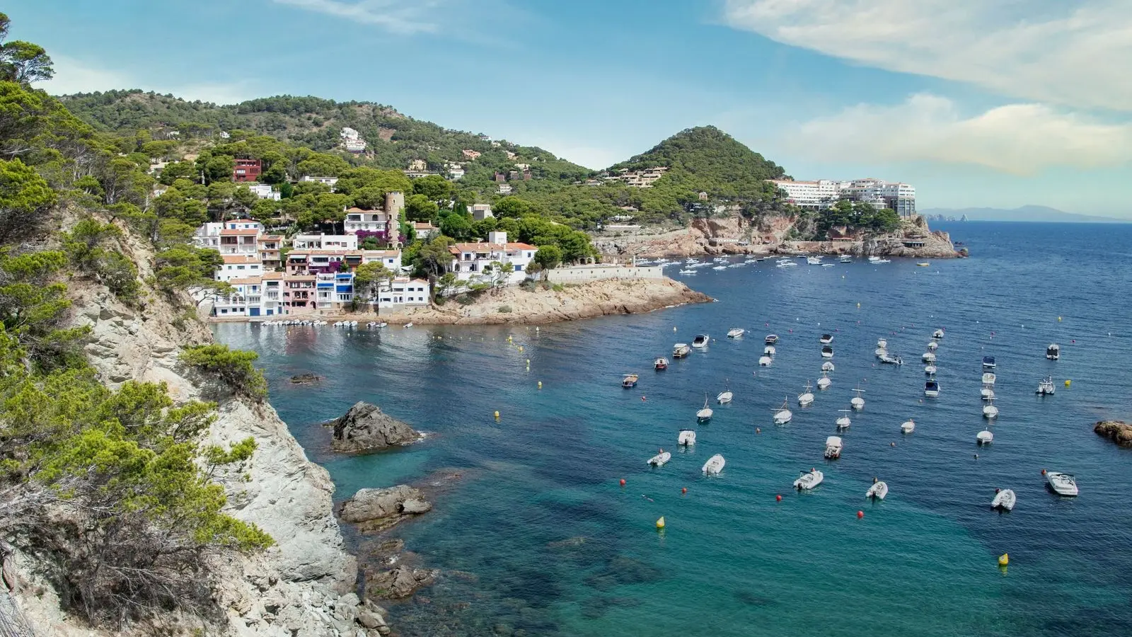 Cala de la Costa Brava con casas en la ladera y barcas fondeadas, como las de la costa de Palamós