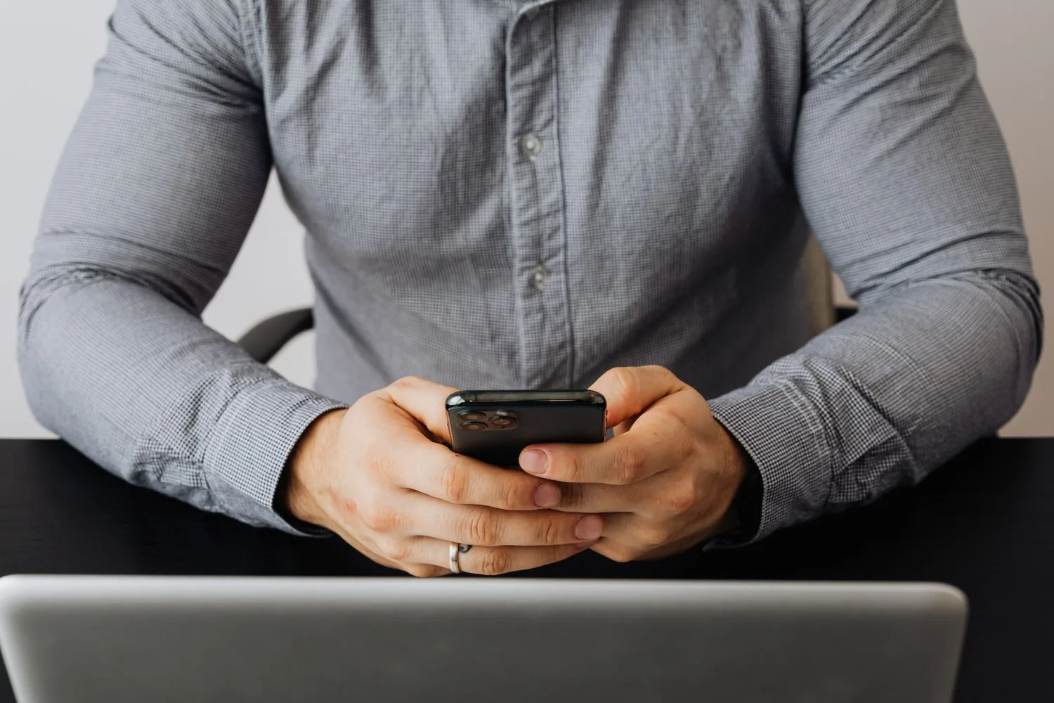 A man in a shirt types on his phone in front of a laptop, like someone asking ChatGPT about a business in their area