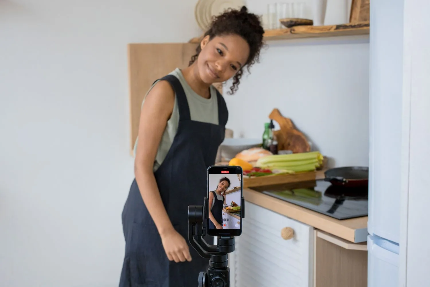 A cook in an apron smiles while filming herself on a phone mounted on a gimbal, next to a counter with vegetables: real content from a business for its social media