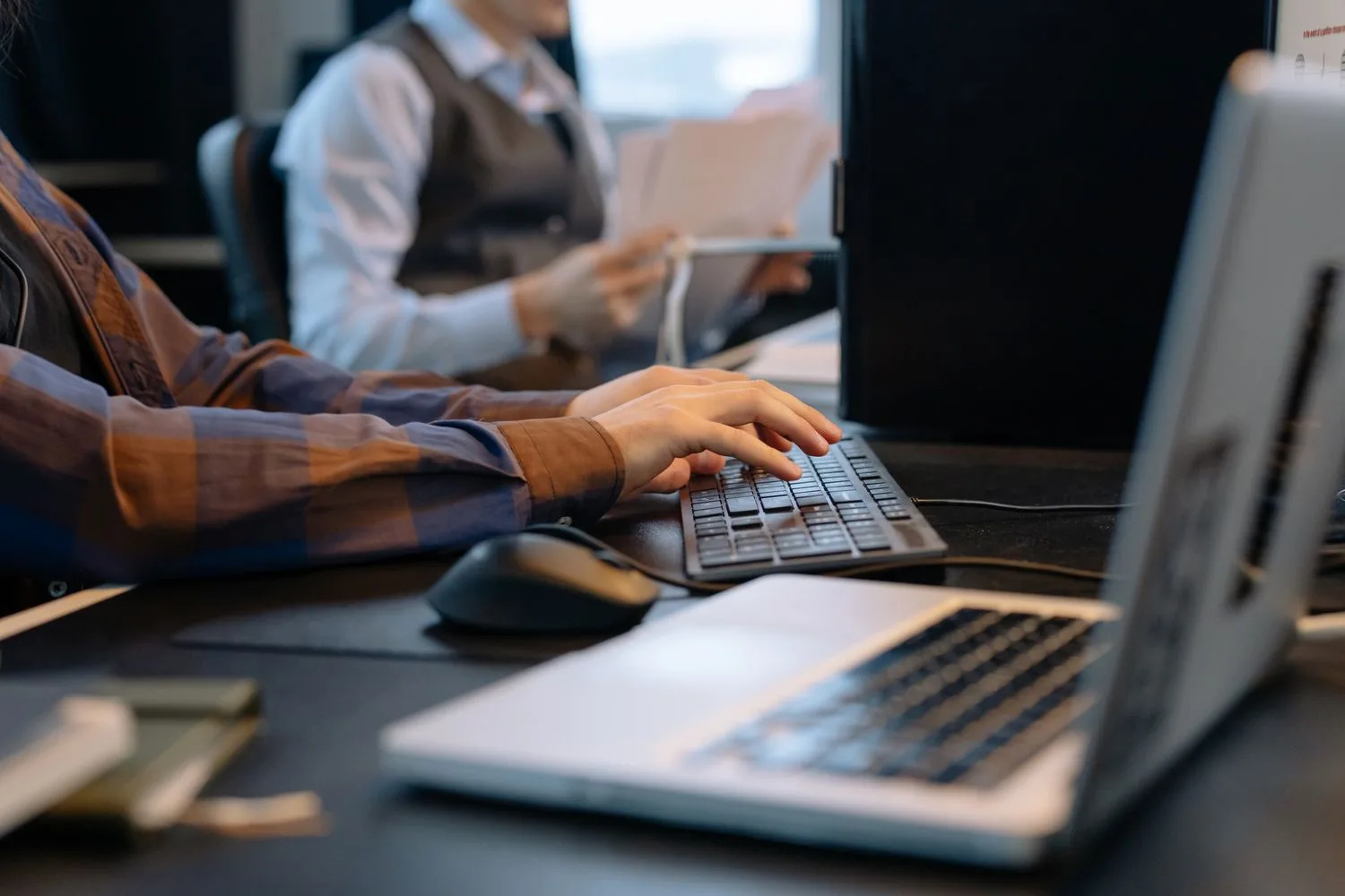 Mans teclejant a l'oficina mentre una altra persona sosté els albarans que cal pujar al portal