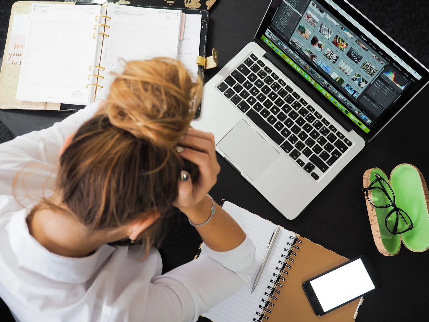 Person overwhelmed at a laptop surrounded by notes, doing the repetitive work that can be automated