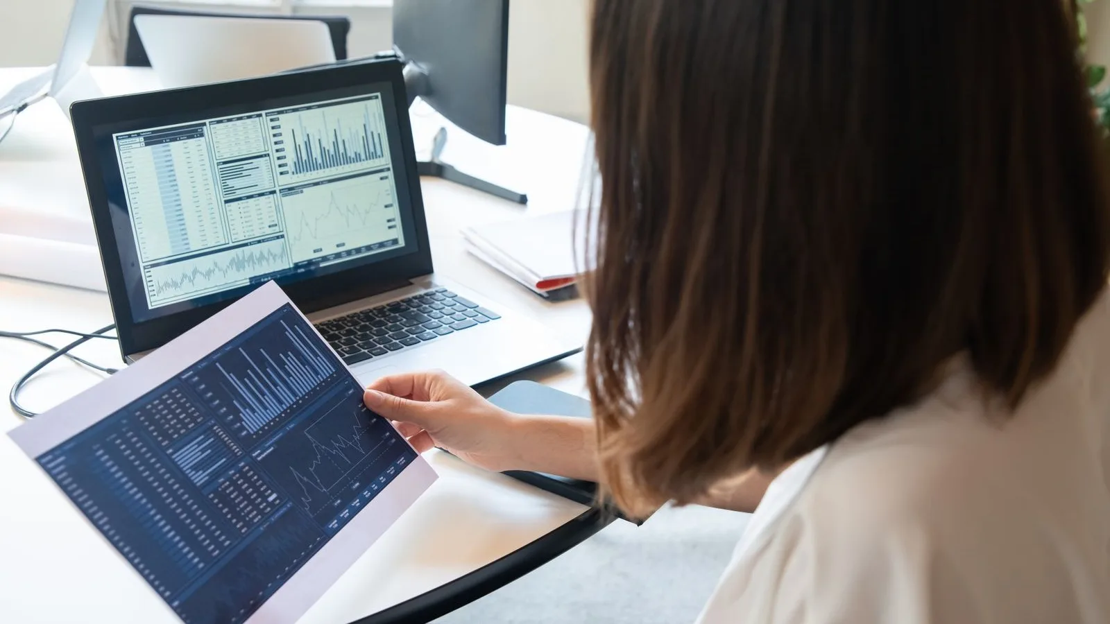 A woman checks website traffic charts on paper and on her laptop, like someone looking at how much ChatGPT and other AI traffic reaches their business