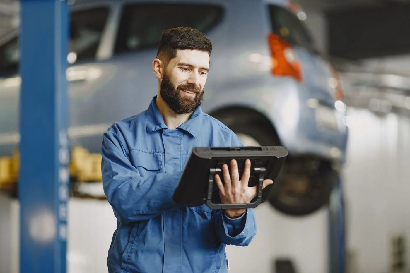 A mechanic using a tablet on his feet next to the car he is repairing