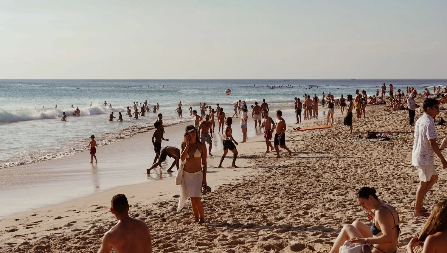 A beach full of people in summer, the tourist who is already in town and decides where to spend on their phone